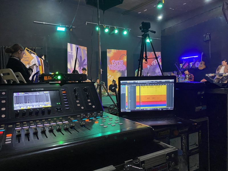 Digital mixing console with multiple faders and LED displays in a concert setup